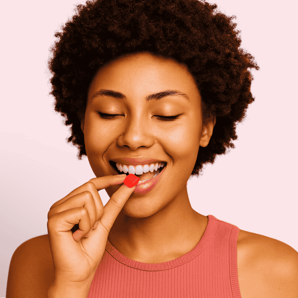 Woman eating a glow up gummy  on a pink background